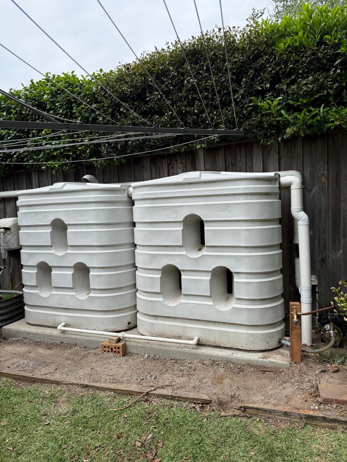 Two slimline rainwater tanks installed by Ready Plumbing against a side fence